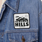 Person wearing a denim jacket with a 'The Black Hills' patch on a white background